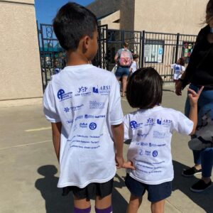 APMC proud sponsor of the La Mariposa School jogathon fundraiser. Image of two small children wearing shirts with sponsorship logos.
